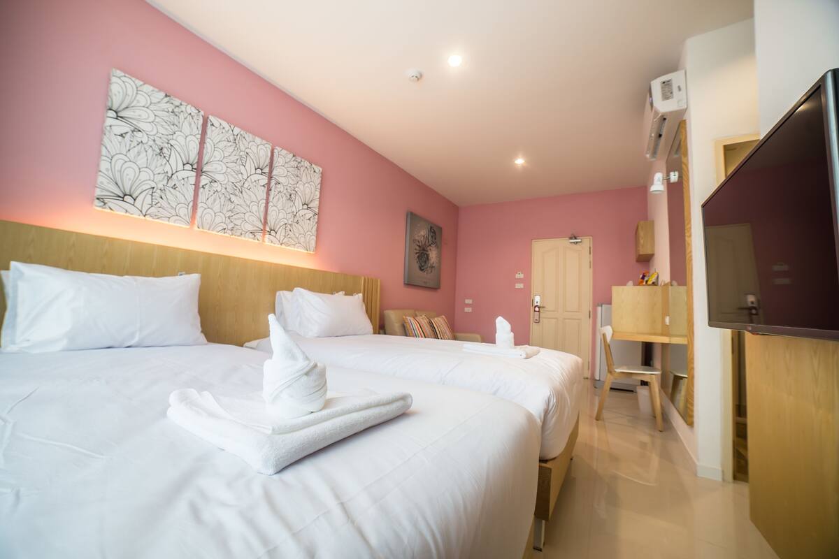 A hotel room with two beds, a wooden headboard, a large artwork on the wall, a wooden desk, and a television.