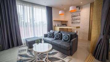 A modern living room with a grey sofa, a round coffee table, and a kitchen area in the background.