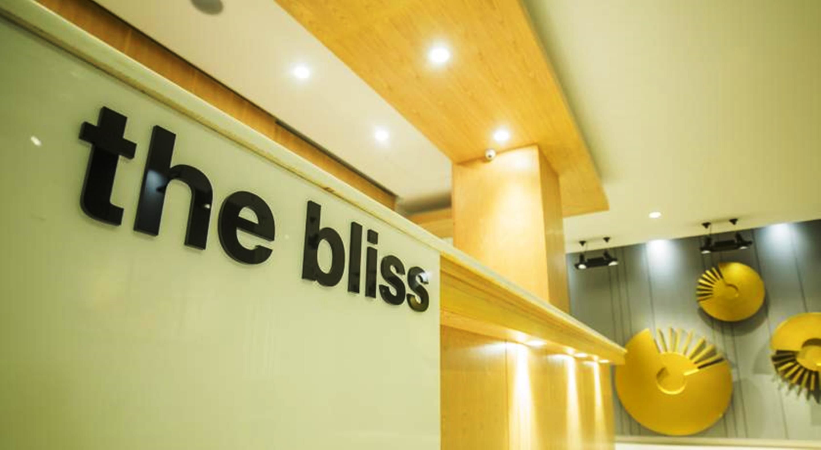 A sign with the text "the bliss" in a modern interior setting with wooden beams and recessed lighting.