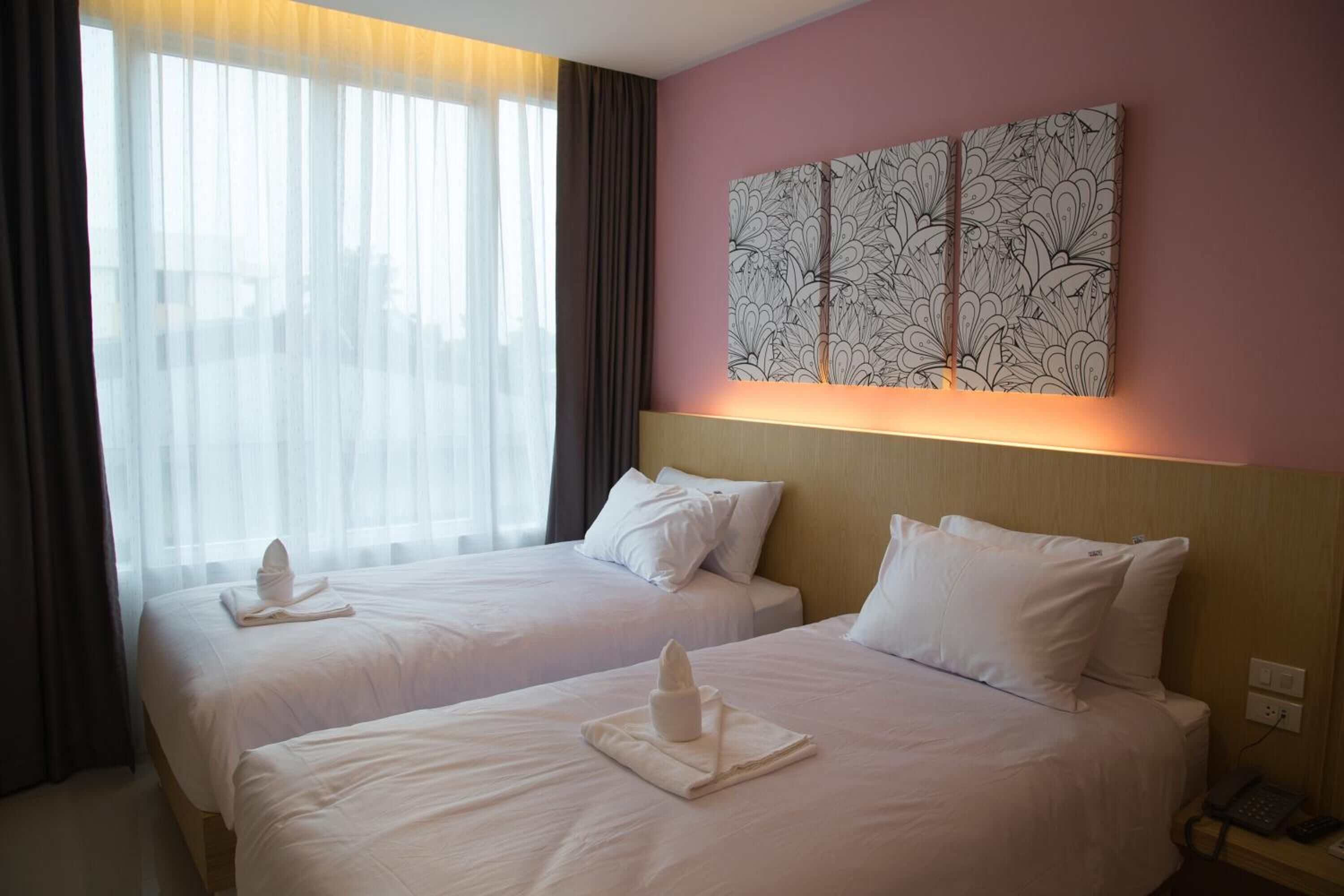 Habitación de hotel con dos camas, un ventanal grande con cortinas translúcidas, una obra de arte en la pared y una mesita de noche con teléfono.
