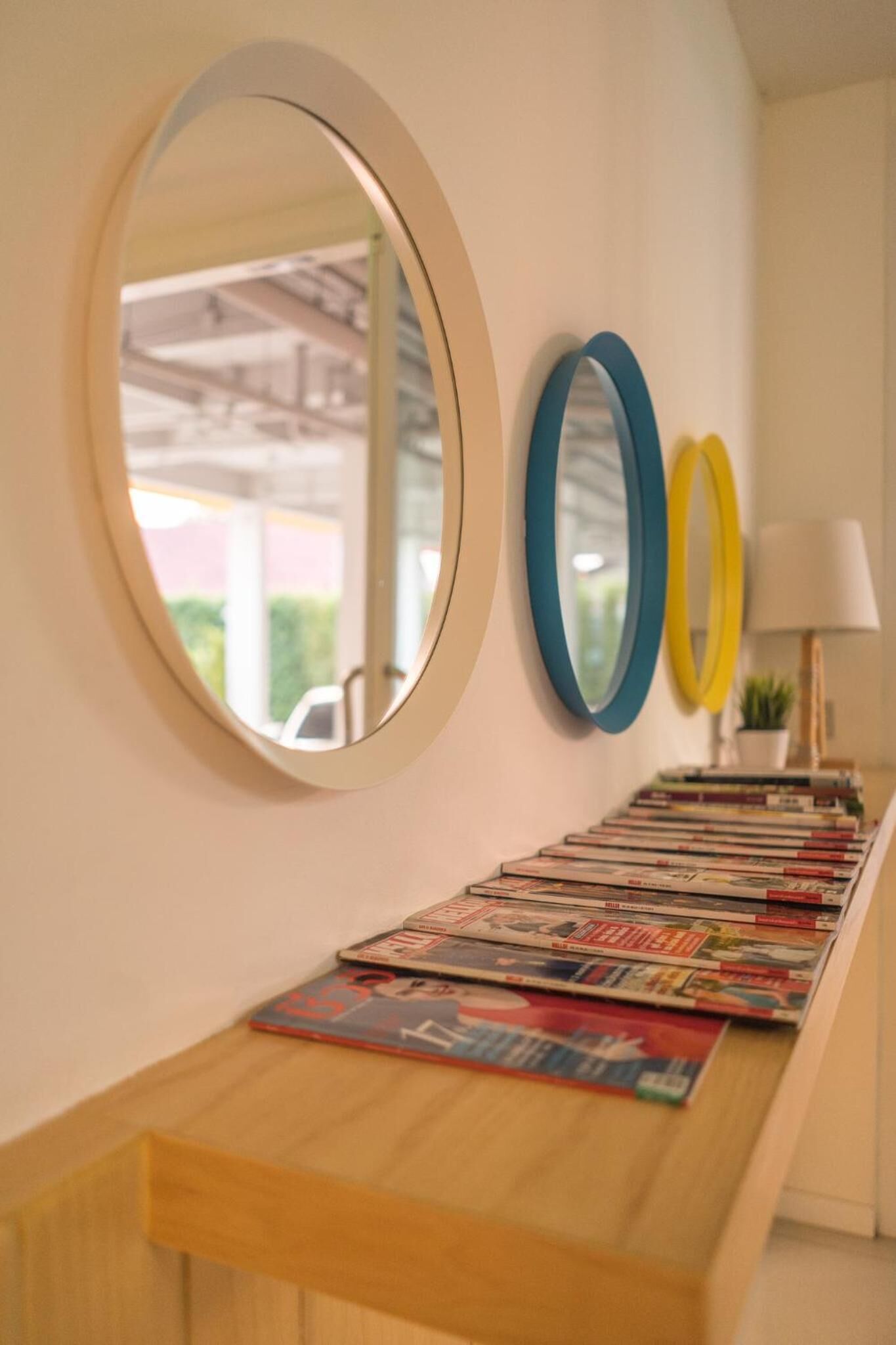 Una pared con tres espejos redondos y un estante de madera con revistas.