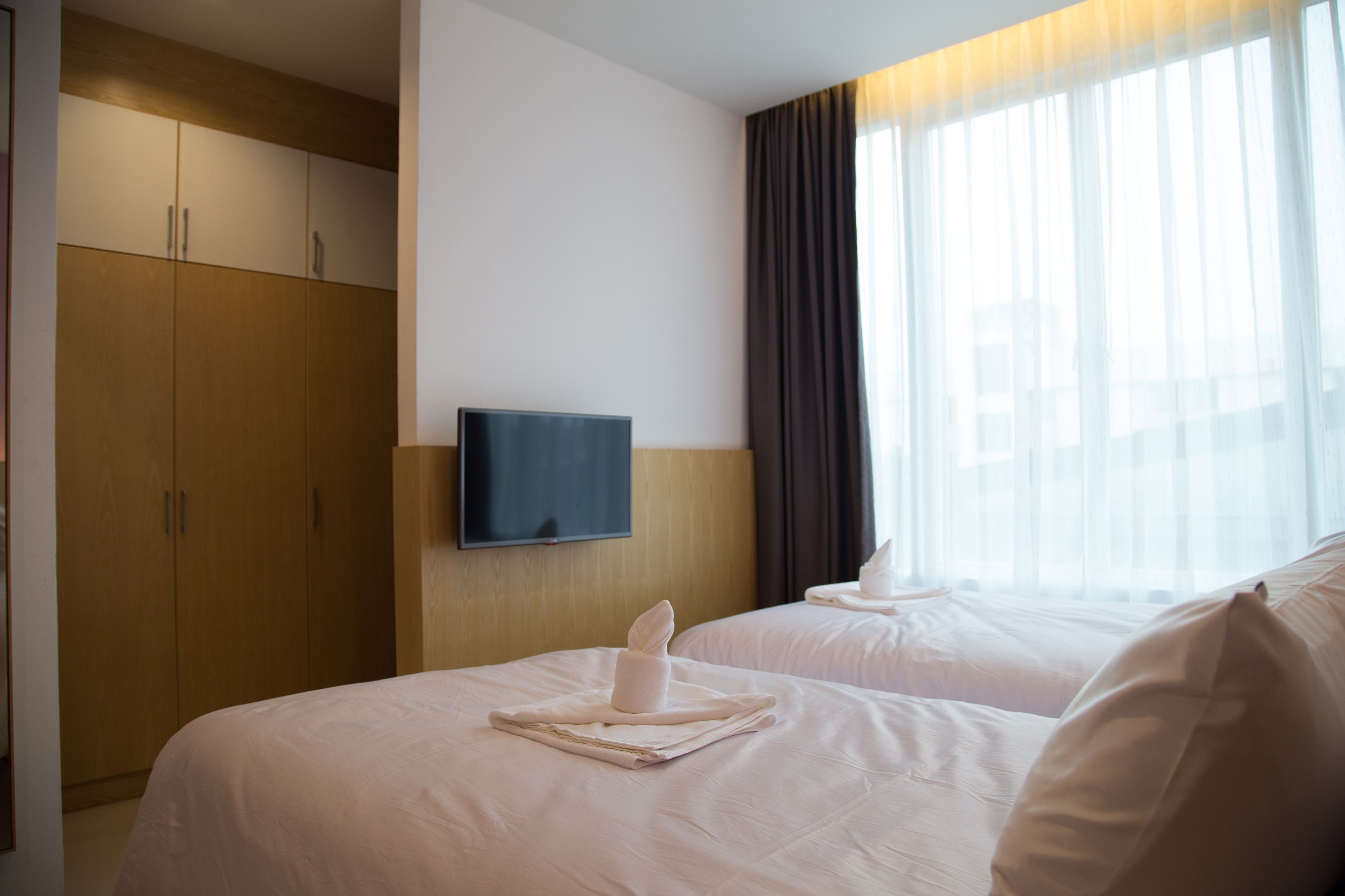 Habitación de hotel con dos camas, un televisor montado en la pared y un armario.