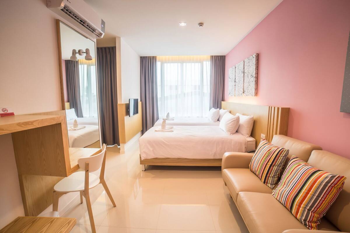 A hotel room with a bed, a desk, a chair, a sofa, and a large window with curtains.