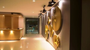 Un hall d’hôtel moderne avec un comptoir d’accueil, une cloison en verre et des horloges décoratives murales.