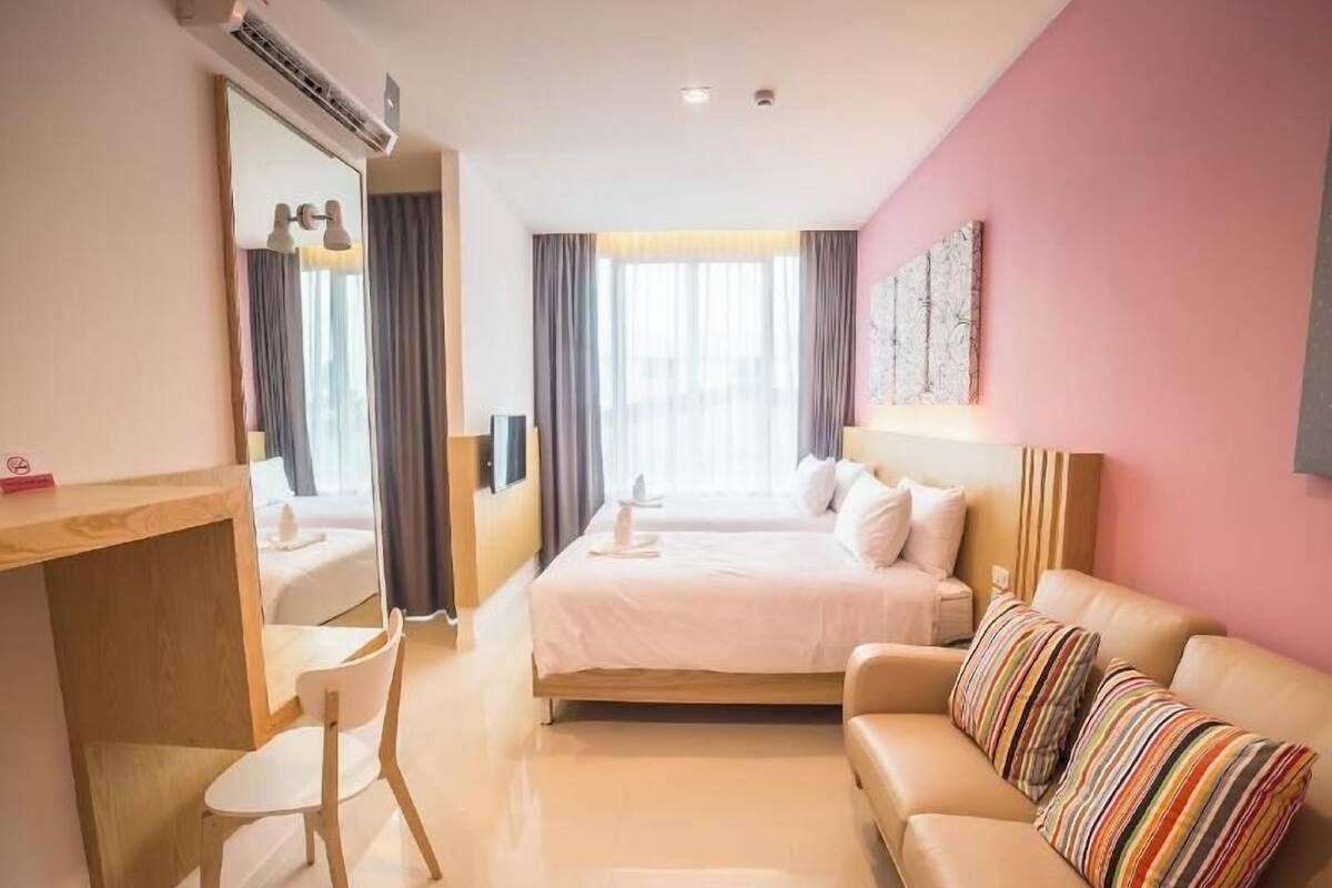 A hotel room with a bed, a desk, a chair, a sofa, and a large window with curtains.