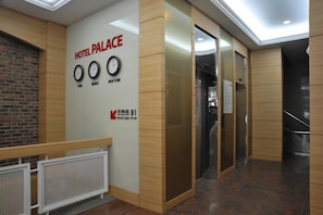 A hotel lobby with a modern design, featuring a wall with clocks indicating different time zones, a reception desk, and a staircase leading to other floors.