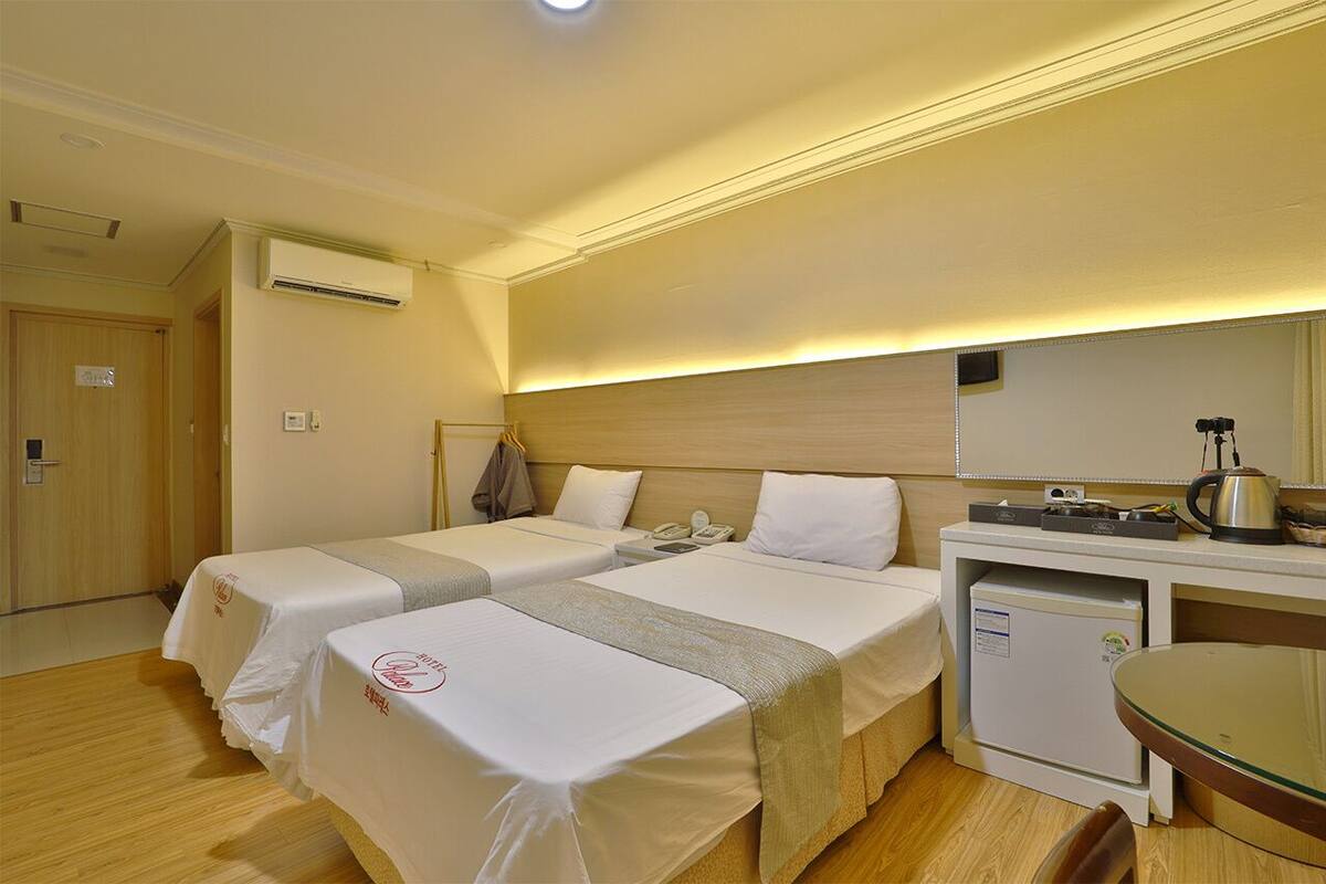 A hotel room with two beds, a small kitchenette, a desk, and a dining table.