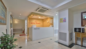 A hotel reception area with a front desk, a clock, and a microwave on a small table.