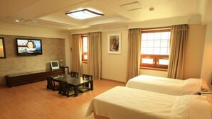 A hotel room with two beds, a TV, a desk, and a window with curtains.