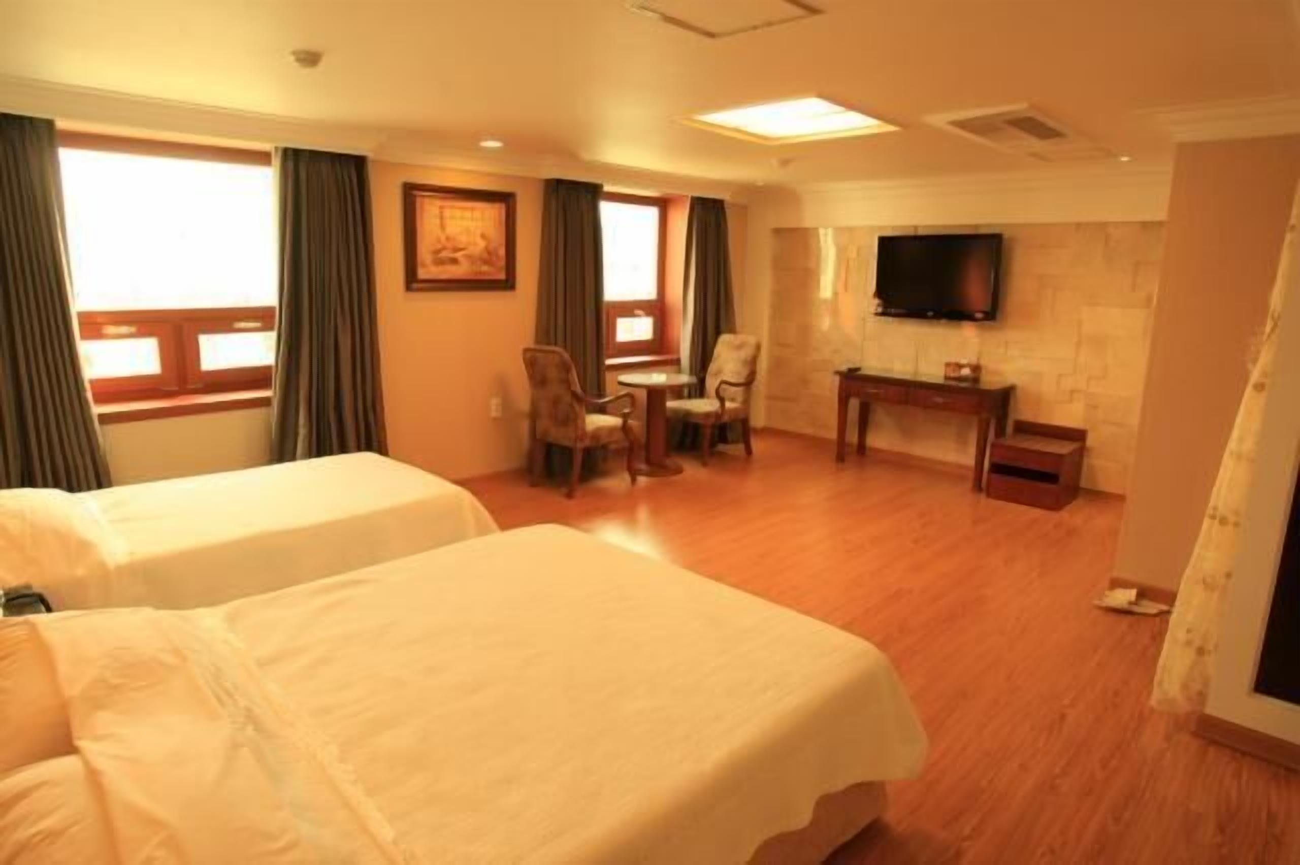 A hotel room with two beds, a desk, a chair, a television, and a window with curtains.
