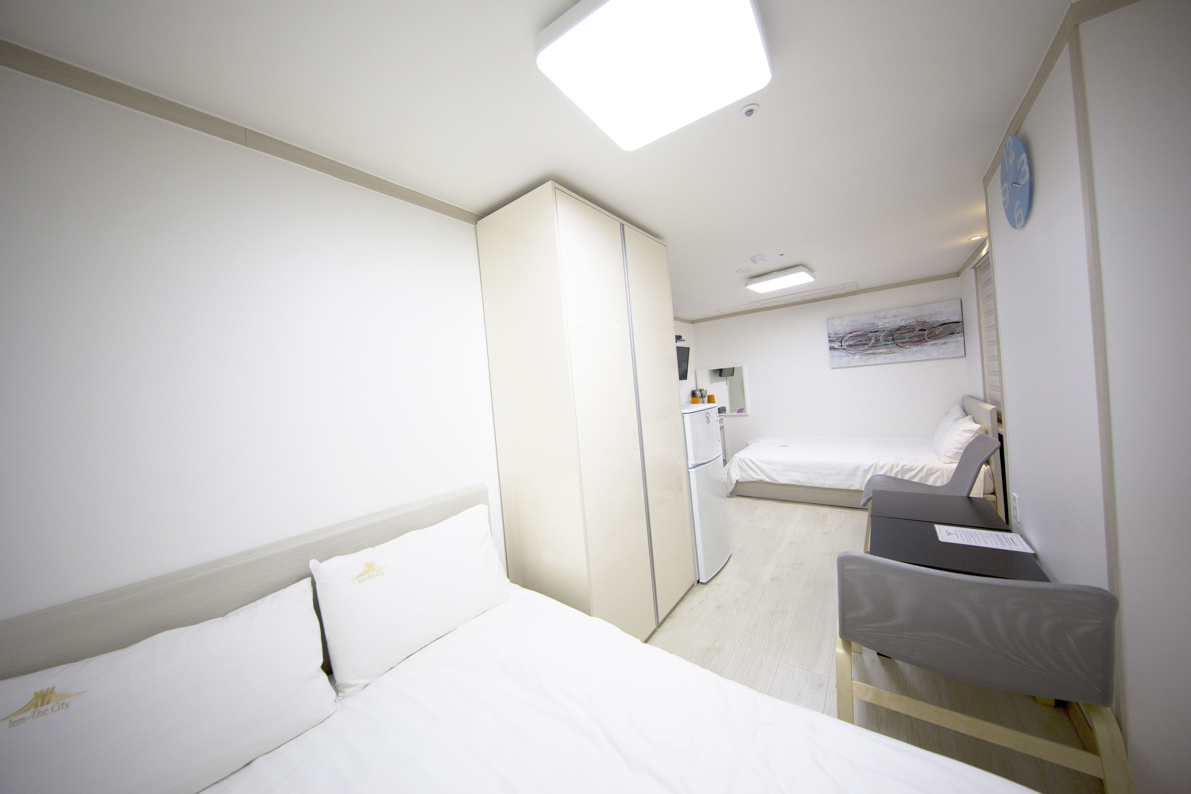 A hotel room with a bed, a desk, a wardrobe, and a small refrigerator.