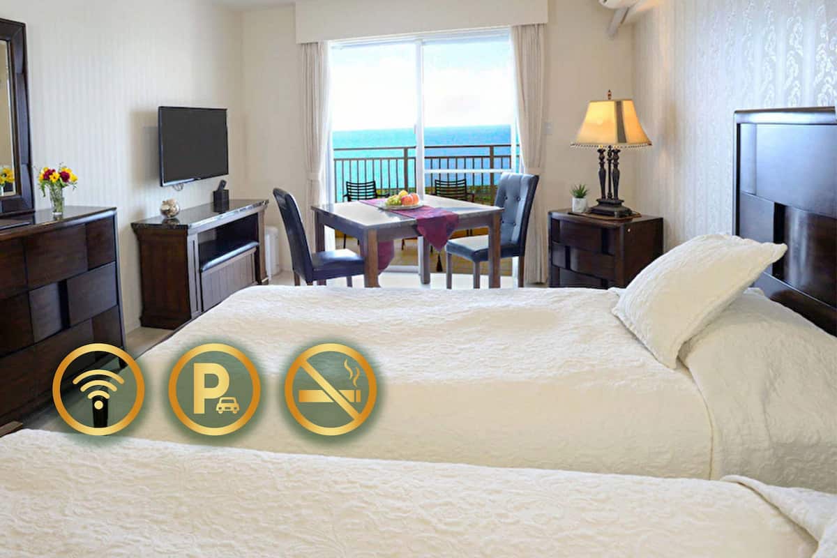 A hotel room with a bed, a desk, a chair, a TV, and a balcony with a view of the sea.