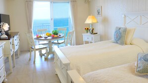 Habitación de hotel con cama, una mesa de comedor con sillas, una lámpara y vista al mar.