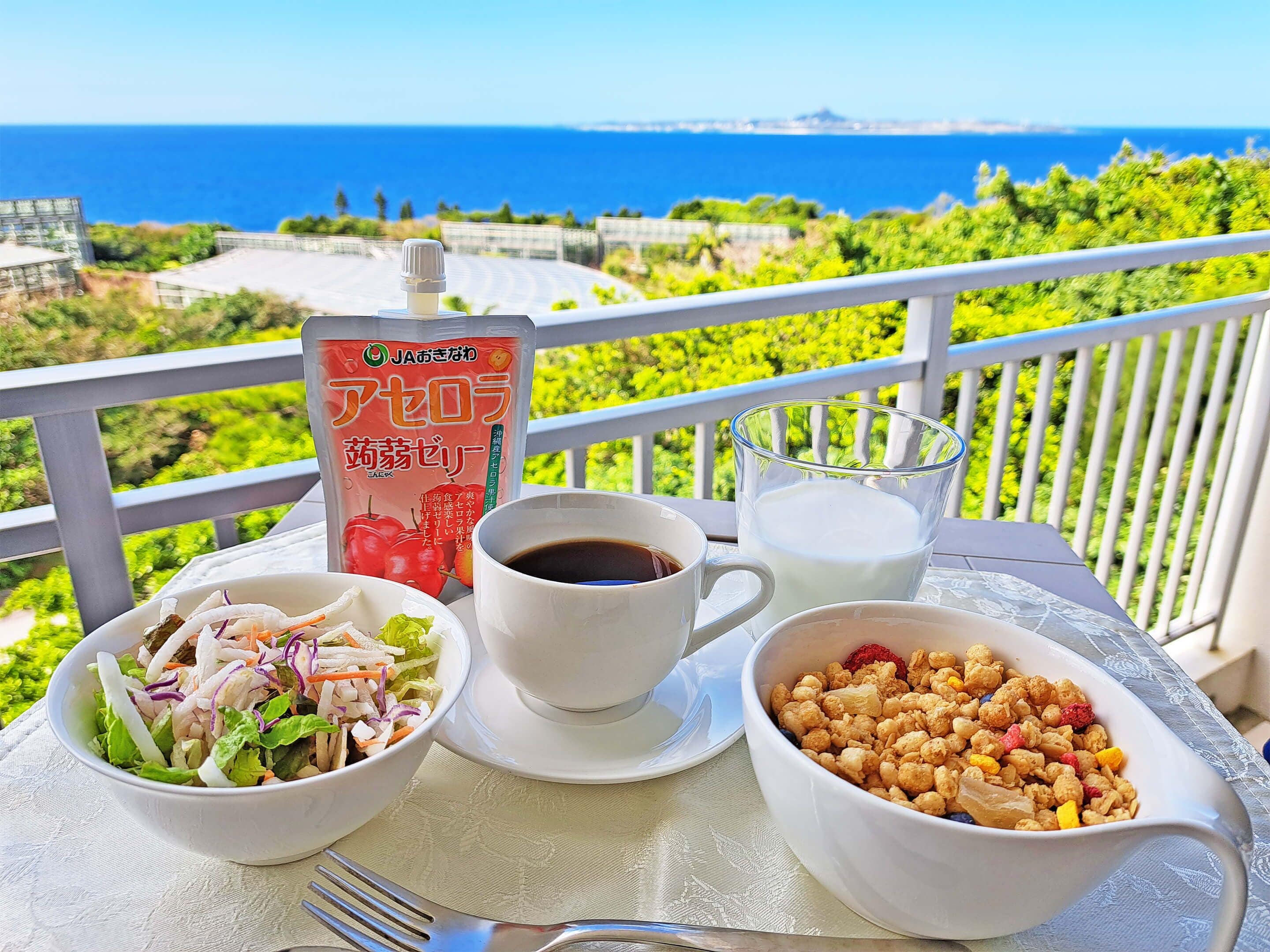 A table with a salad, coffee, milk, and a snack bowl on a balcony with a view of the sea.
