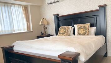 A neatly made bed with a dark wooden headboard, a bedside table with a lamp, and a wall-mounted air conditioner.