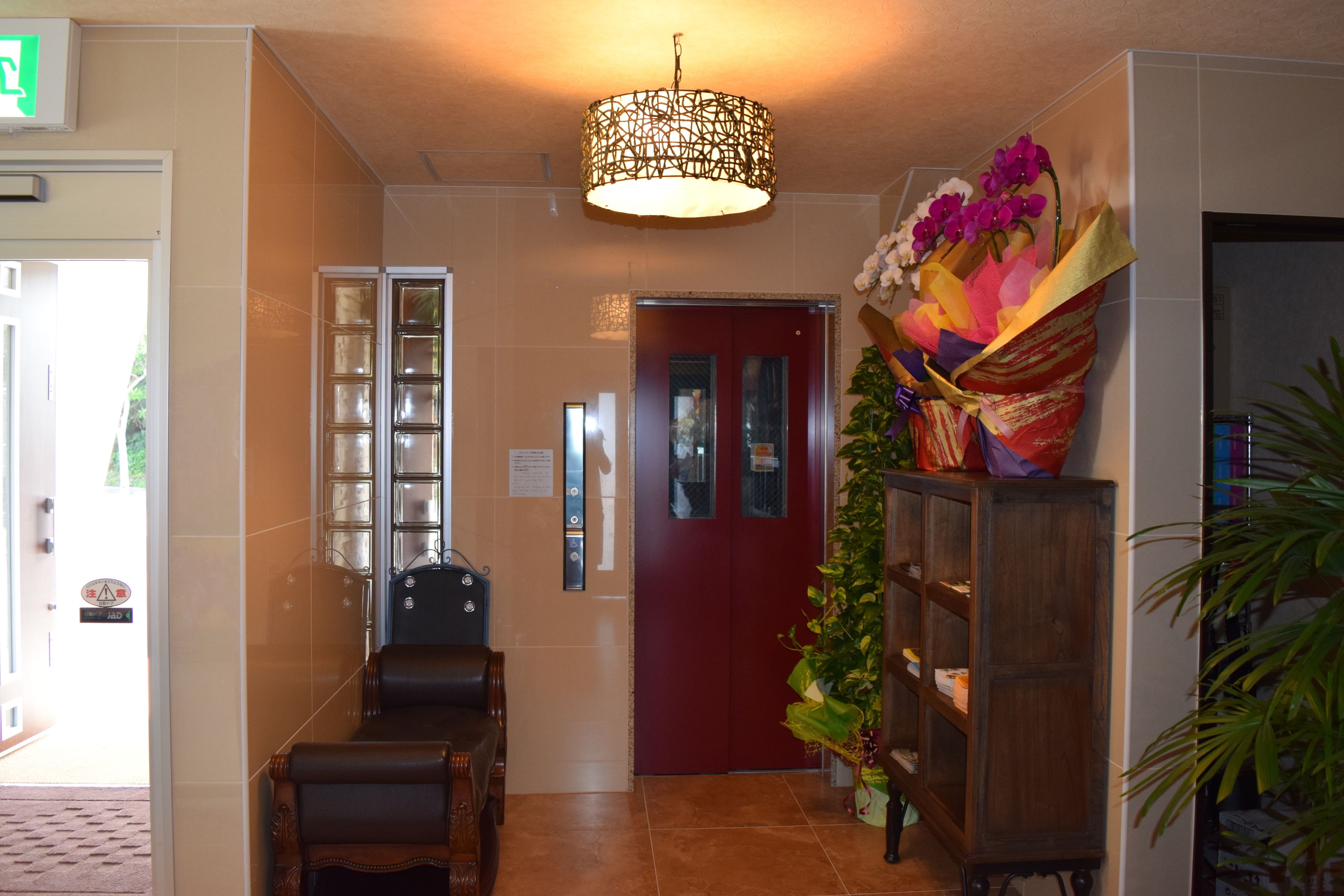 Una hall con una reception, una porta rossa, una pianta sospesa al muro e un lampadario.