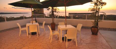 An outdoor patio with white chairs and tables, two umbrellas, and potted plants.