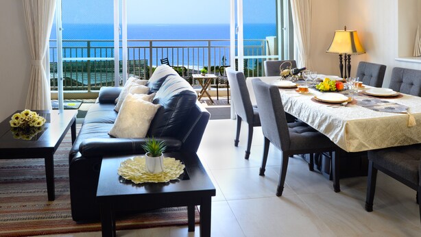 Un comedor con una mesa lista para cuatro, un sofá y vista al océano.