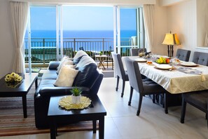 A dining area with a table set for four, a sofa, and a view of the ocean. - Wisteria Condominium Resort (Motobu)