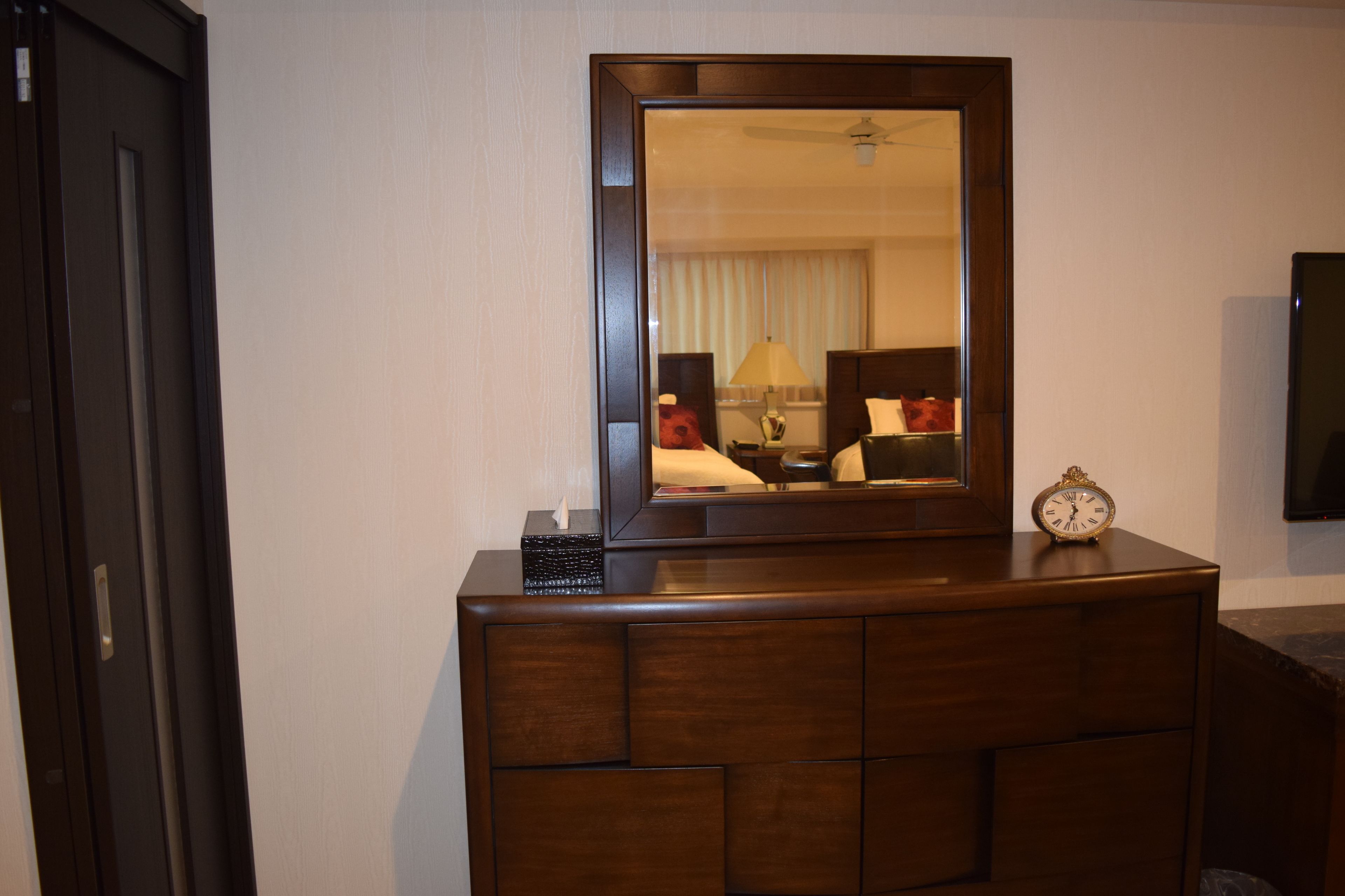 A wooden dresser with a mirror, a clock, and a tissue box.