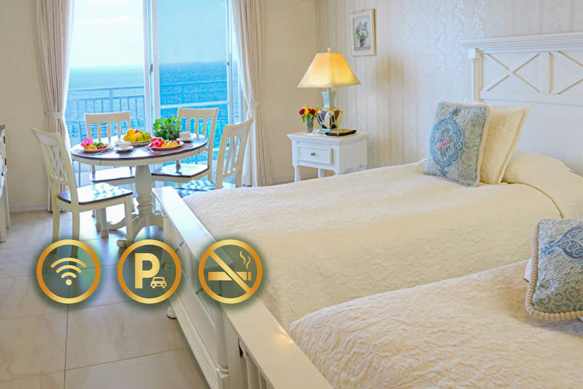 A hotel room with a bed, a dining table with chairs, a lamp, and a view of the ocean.