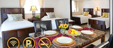 A hotel room with a large bed, a smaller bed, a dining table set for two, and a mirror reflecting the room.