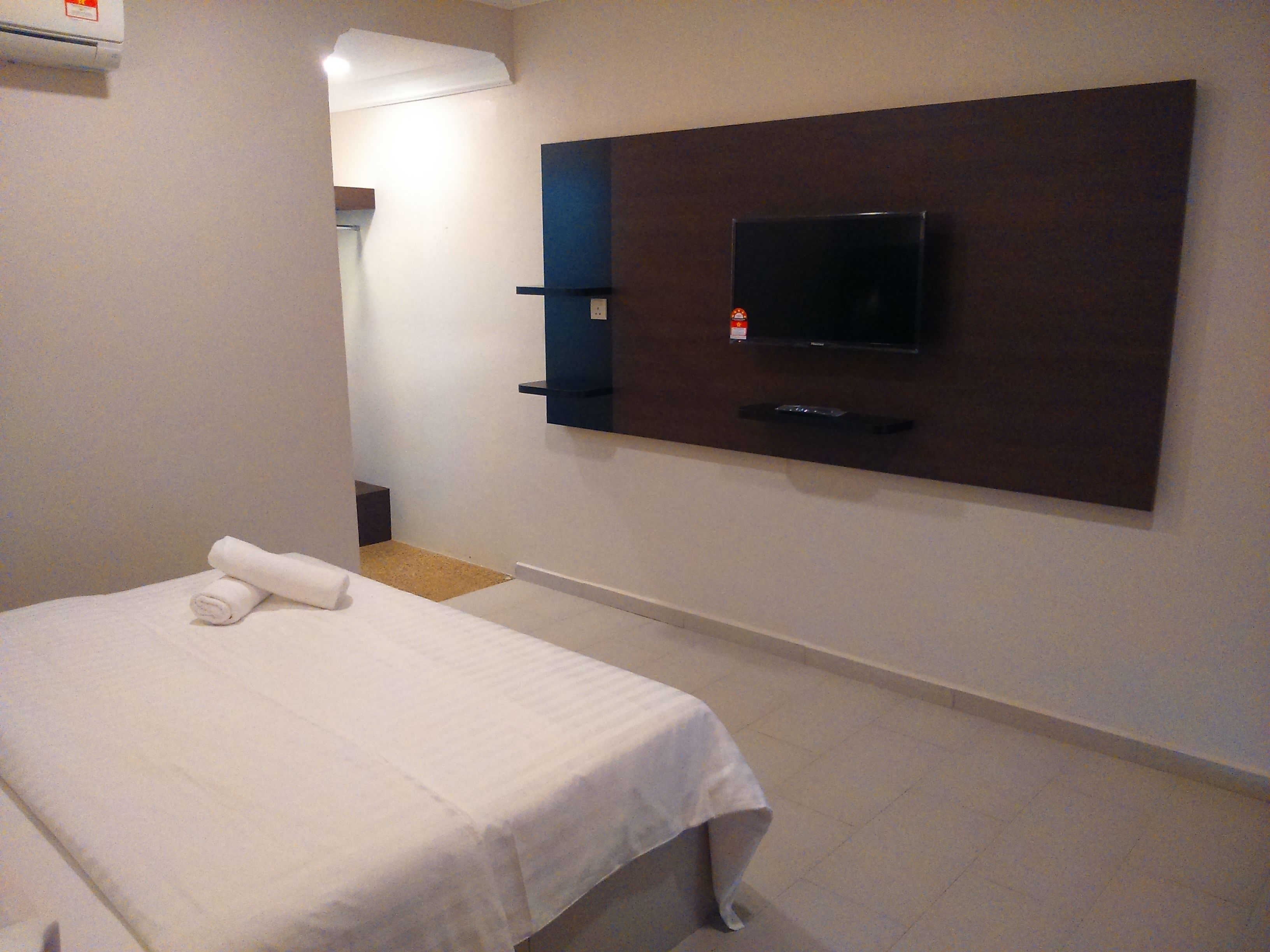 A hotel room with a bed, a flat-screen TV mounted on the wall, and a small bedside table.