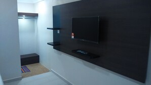 Ein modernes Zimmer mit einem an einer dunklen Wand montierten Flachbildfernseher, einer kleinen Ablage darunter und einer Tür zu einem weiteren Raum.