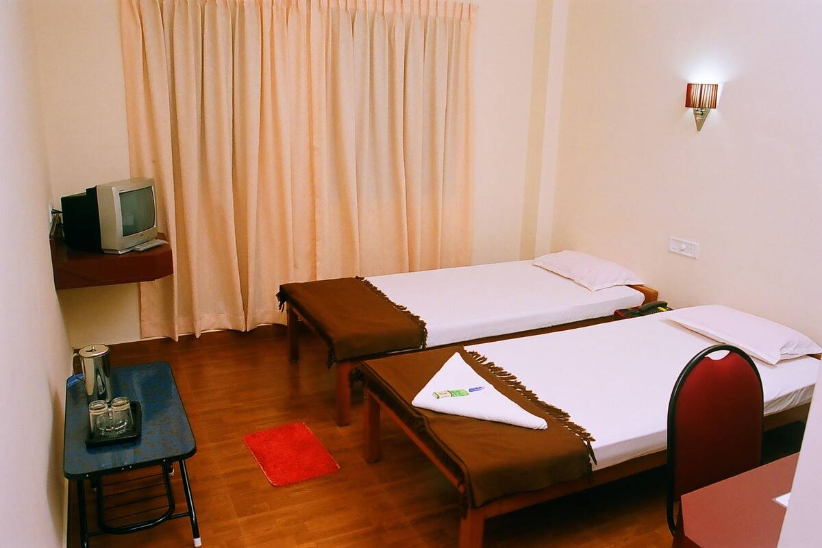 A hotel room with two single beds, a small desk with a television, and a red rug on the floor.