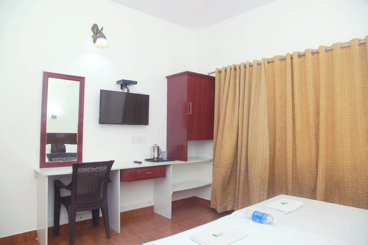 A hotel room with a desk, chair, television, wardrobe, and a bed with a curtain.