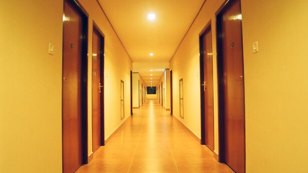 A long, narrow hotel corridor with wooden doors on both sides and a tiled floor. - Hotel Srinivas (Kanayannur)