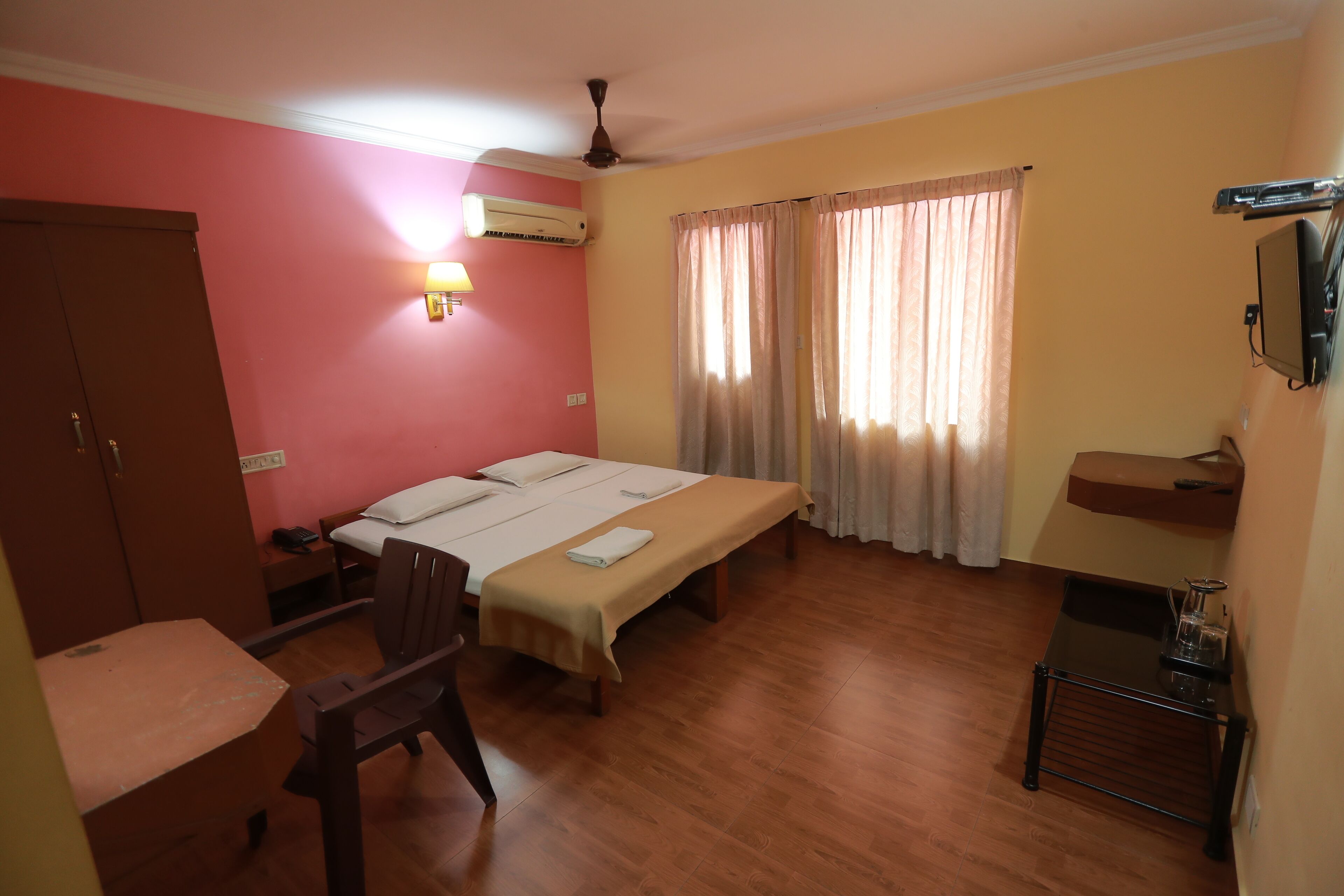Una habitación con cama, escritorio, silla, aire acondicionado, televisor y ventana con cortinas.