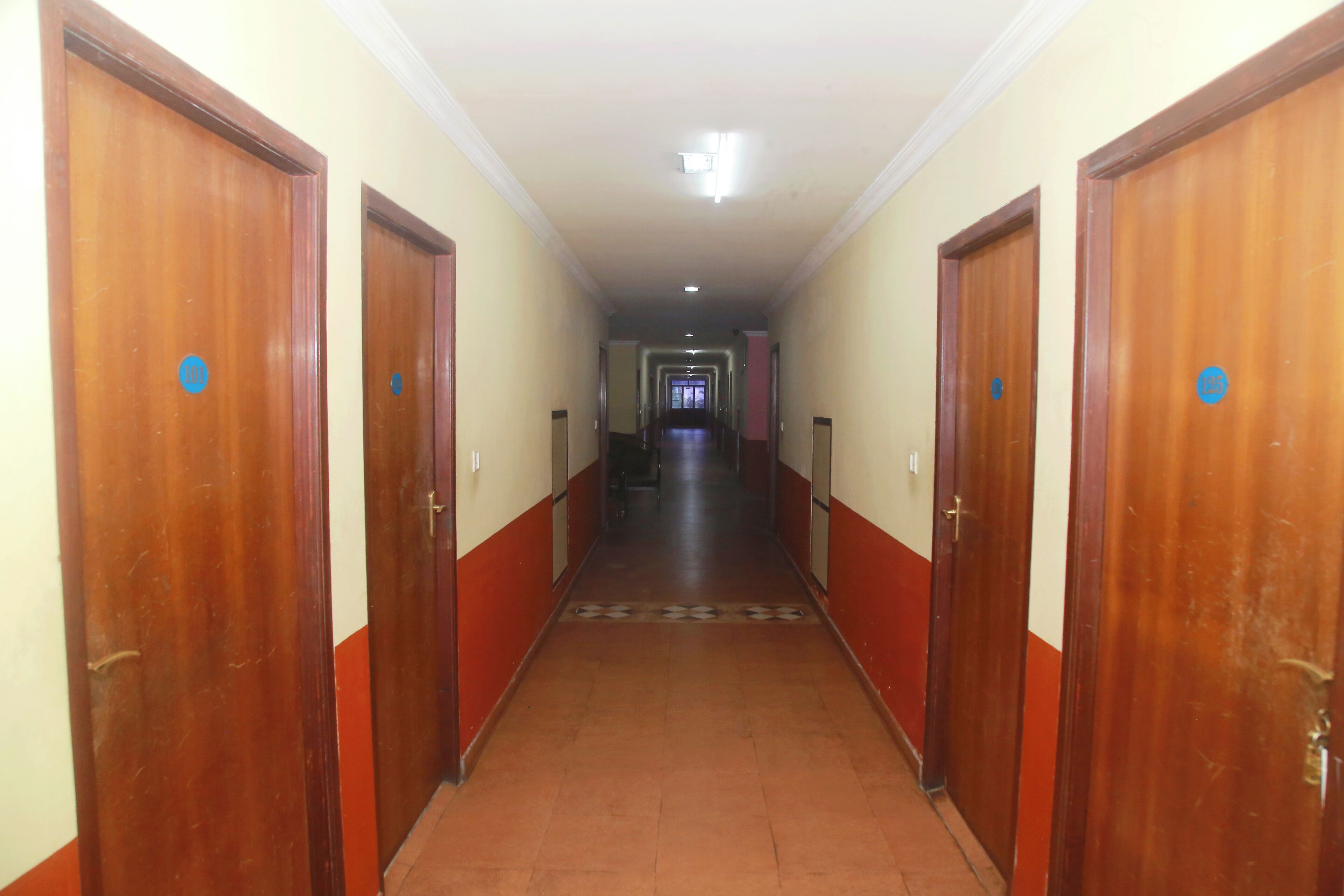 Un pasillo con puertas de madera numeradas que conduce a un vestíbulo con suelo de baldosas.