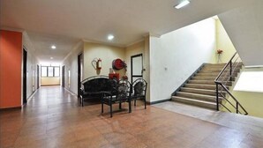 A spacious hallway with a staircase on the right, a black sofa, and a fire extinguisher on the wall. - Hotel Srinivas (Kanayannur)