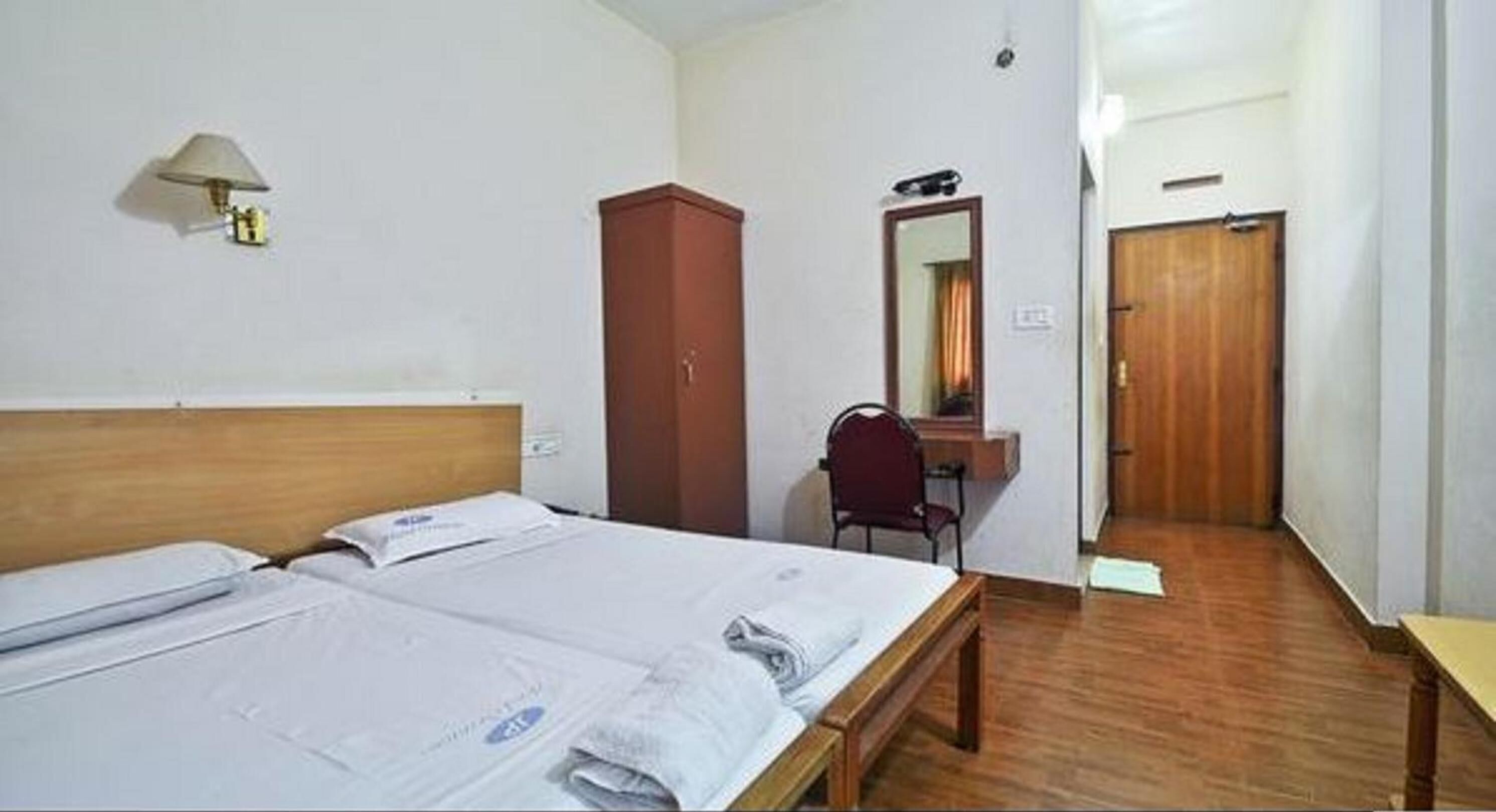 Habitación de hotel con dos camas, un escritorio, una silla, un armario y un espejo.