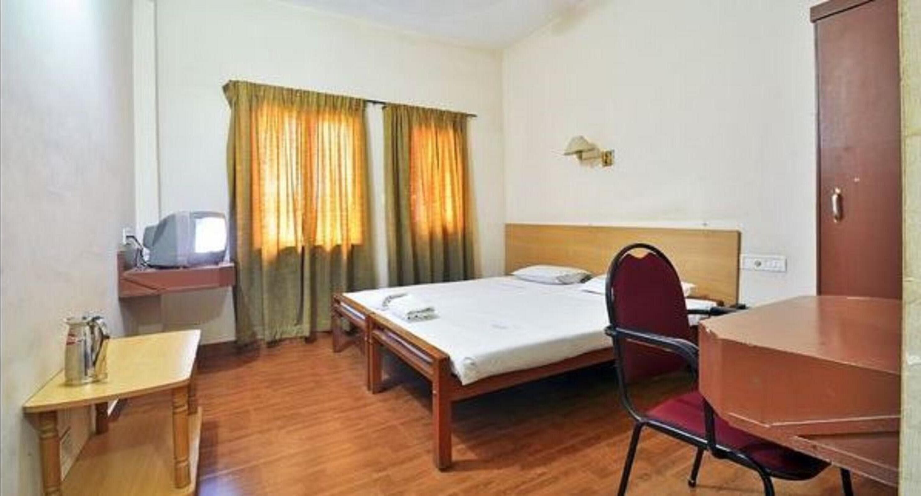 A hotel room with a wooden floor, a single bed, a desk with a chair, a small table, and a television.