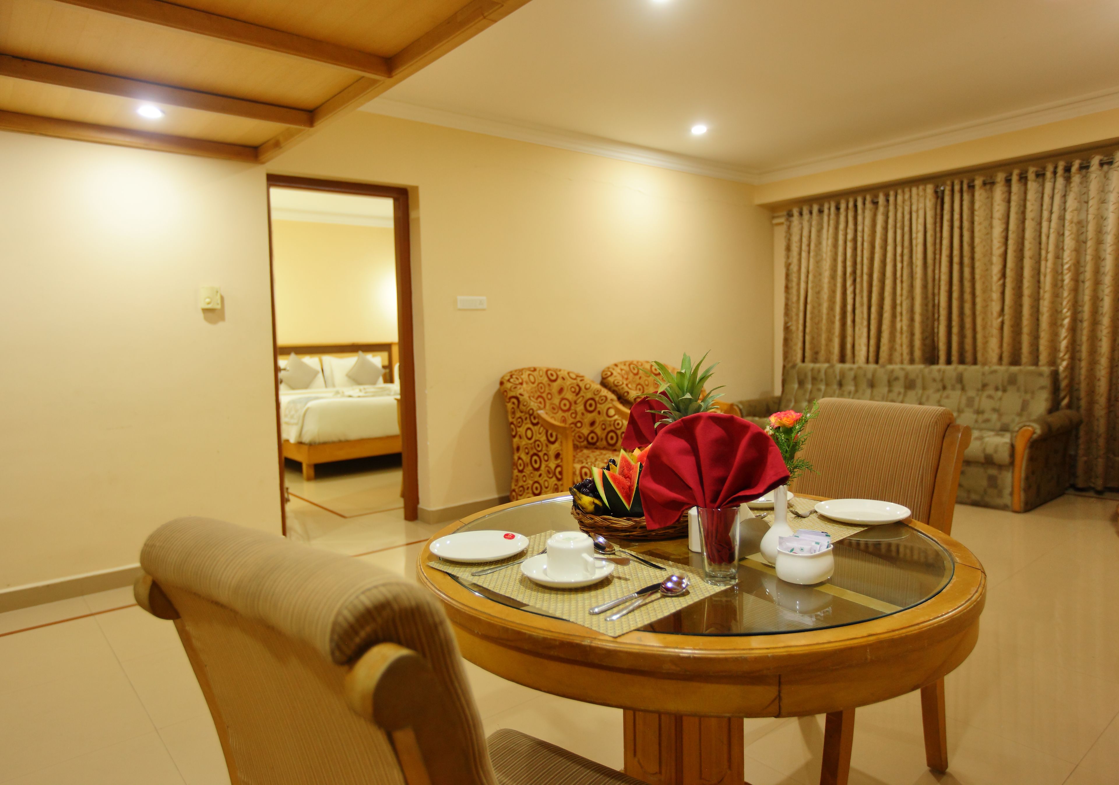 A hotel room with a dining table set for two, a sofa, and a bed visible through an open door.