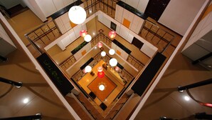 A high-ceiling atrium with a central open space, surrounded by balconies and railings, and multiple hanging light fixtures. - The Dunes Continental (Kanayannur)