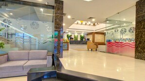 A modern hotel lobby with a reception desk, a seating area with a sofa, and a staircase leading to upper floors. - The Dunes Continental (Kanayannur)