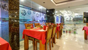 A restaurant with marble walls, red tablecloths, and wooden chairs. - The Dunes Continental (Kanayannur)