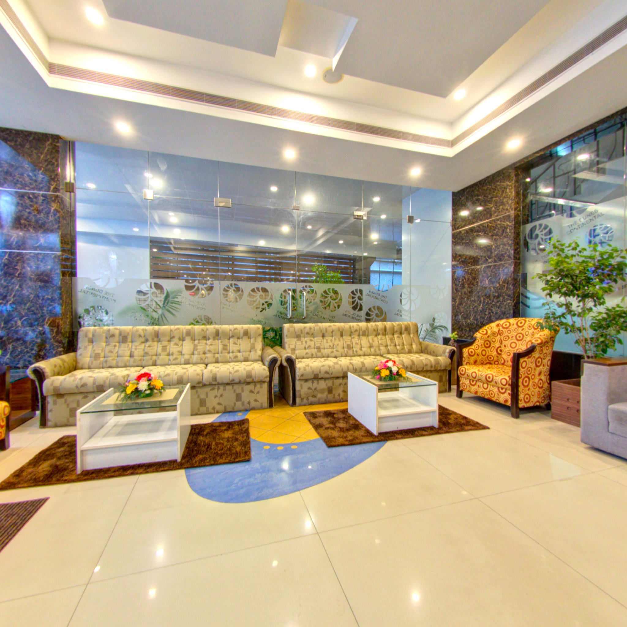 A modern lobby with two sofas, a patterned armchair, and a glass coffee table.