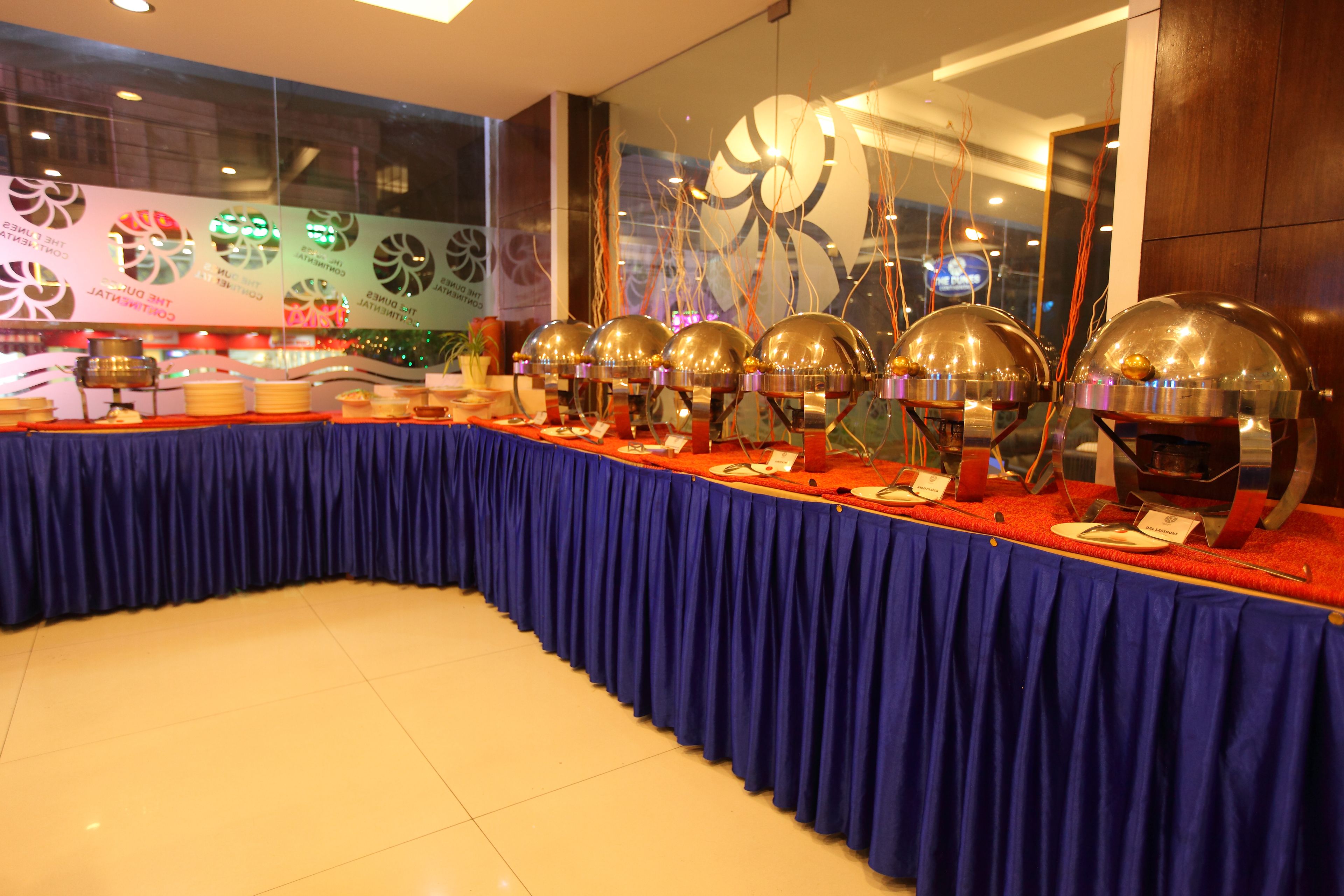 A buffet setup with multiple serving stations, a blue tablecloth, and a decorative backdrop.