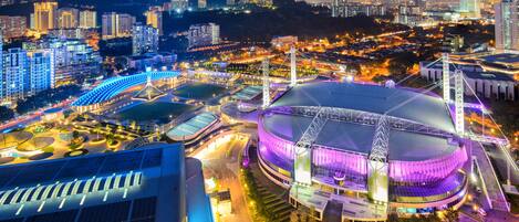 Un estadio con una gran cúpula central y zonas de asientos circundantes, rodeado de edificios urbanos y montañas al fondo.
