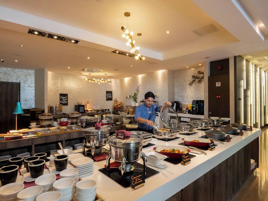 A buffet setup with various food containers and a person serving food.