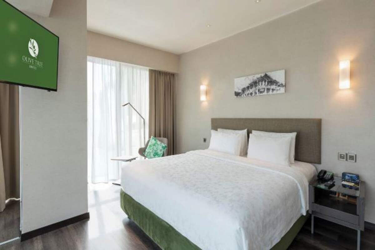 A hotel room with a large bed, a flat-screen TV, a painting on the wall, and a nightstand with a phone and books.