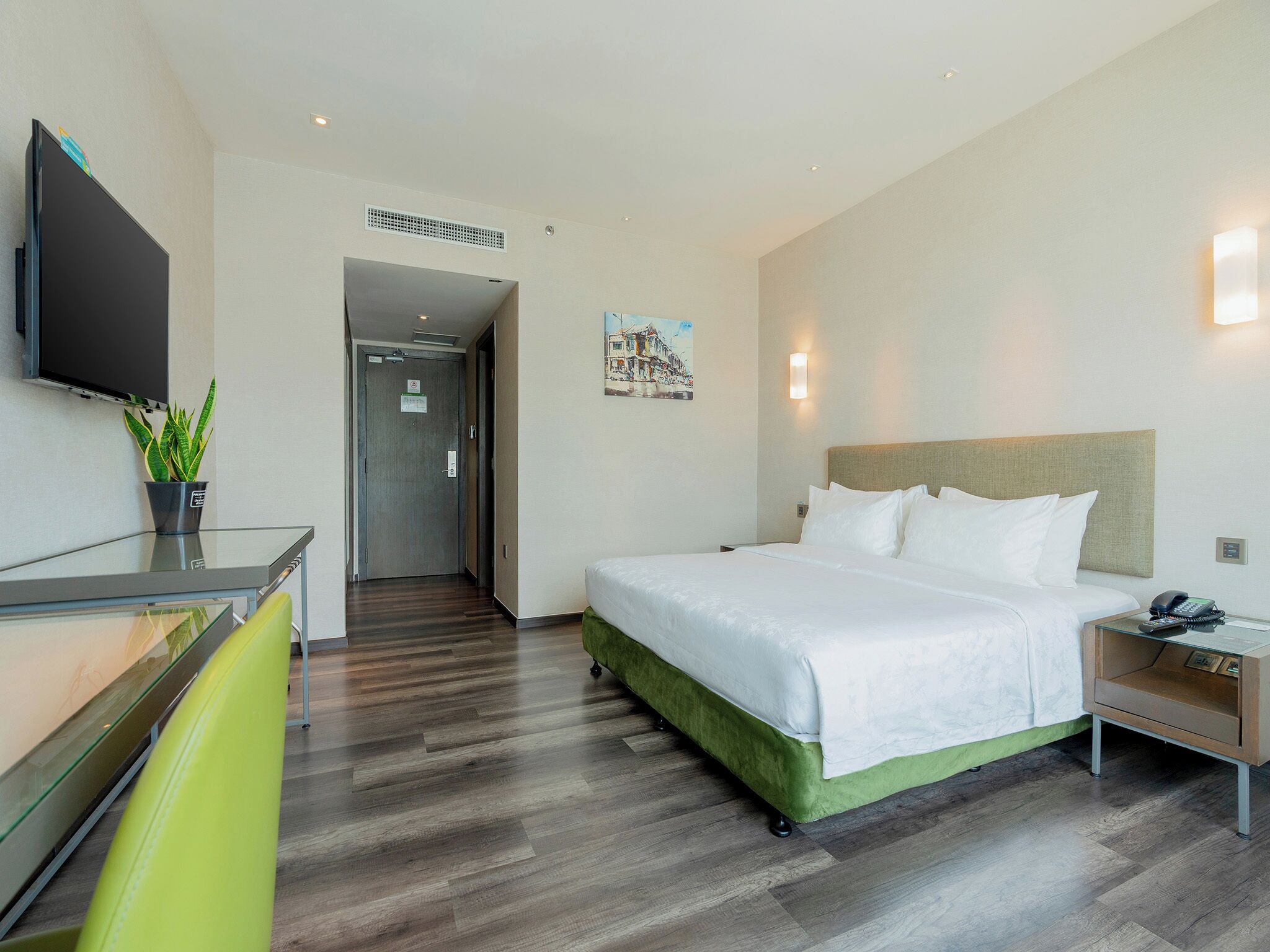 A hotel room with a bed, bedside table, and a flat-screen TV mounted on the wall.