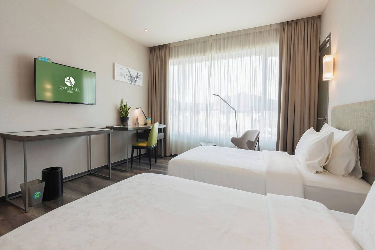 A hotel room with two beds, a desk with a chair, a TV on the wall, and a window with curtains.