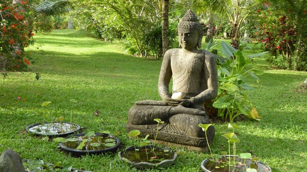 A large stone Buddha statue in a garden with a pond and lotus plants.