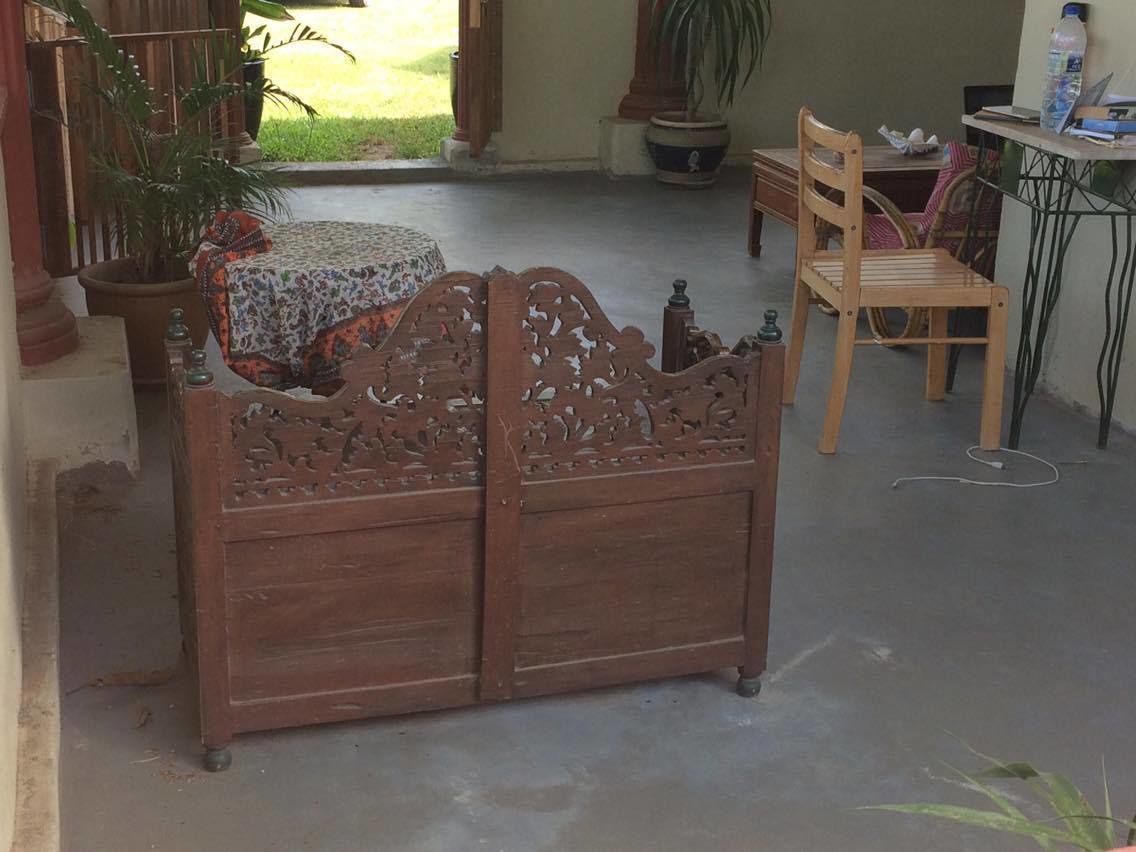 Un banco de madera con intrincados grabados, una mesita con mantel estampado y una silla.