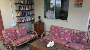 A cozy living room with two patterned sofas, a coffee table, and a bookshelf filled with books. - Bohok Guest House (Langkawi)